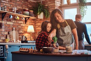 免费照片家庭概念。快乐的妈妈做饭与她的小女儿在阁楼风格的厨房在早晨。