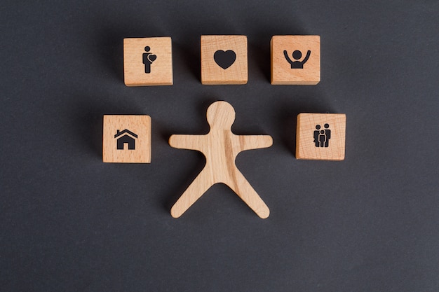 Free photo family concept with icons on wooden cubes, human figure on dark grey table flat lay.