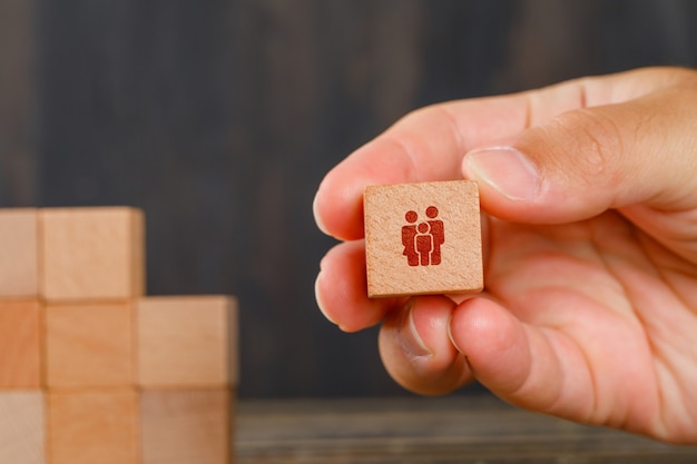 Family concept on wooden table side view. hand holding wooden cube.