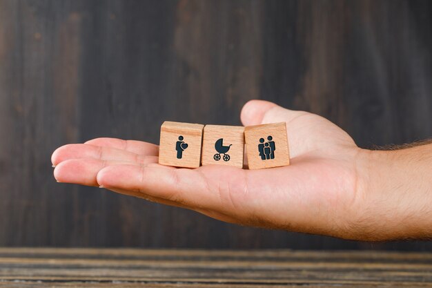 Family concept on wooden table side view. hand holding wooden cubes with icons.