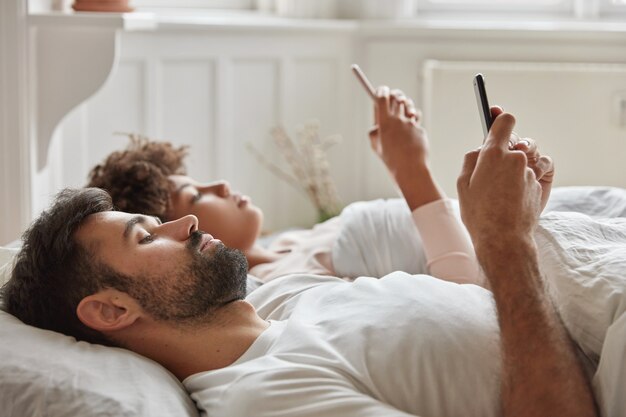 Family couple ignore lively talk before sleep, use smart phone, watch video