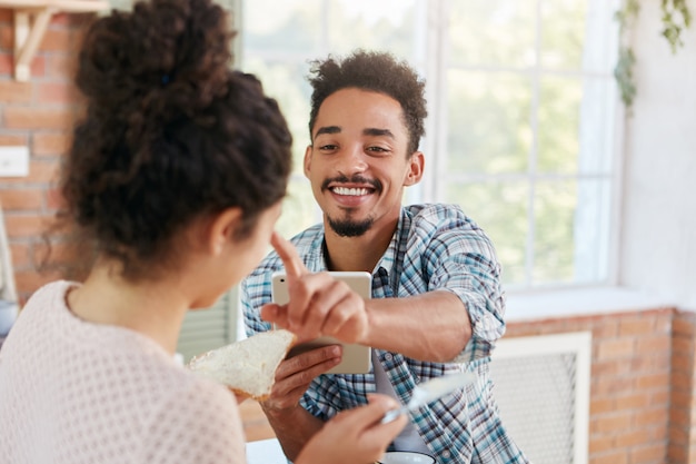 Family couple makes fun at kitchen during lunch: bearded man touches nose of girlfriend who makes sandwiches, feels great love and sympathy.