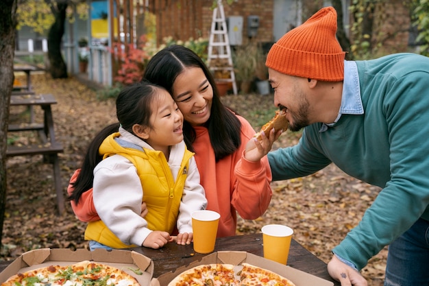 Family eating pizza outdoors medium shot