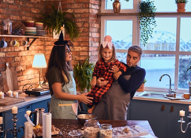 Family in halloween. Mom dad and little daughter with makeup and hats cooking together in loft style kitchen at morning.