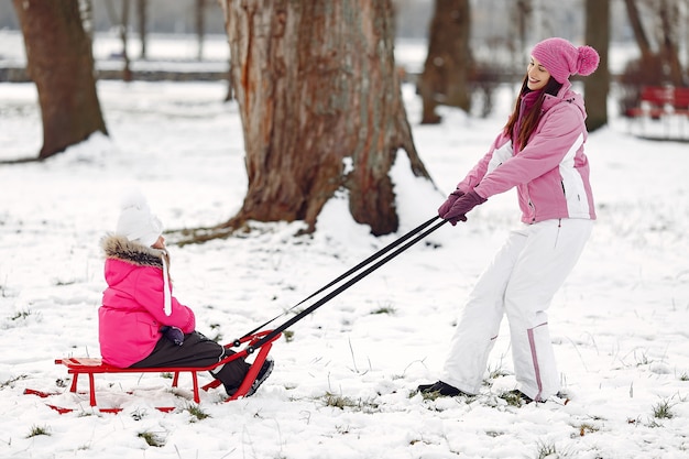 Family in knitted winter hats on family Christmas vacation. Woman and little girl in a park. People playing with sled.