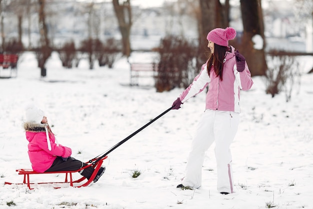 家族のクリスマス休暇にニットの冬の帽子をかぶった家族。公園の女性と少女。そりで遊ぶ人。