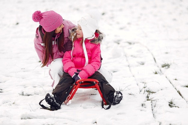 Семья в вязаных зимних шапках на семейных рождественских каникулах. Женщина и маленькая девочка в парке. Люди играют с санками.