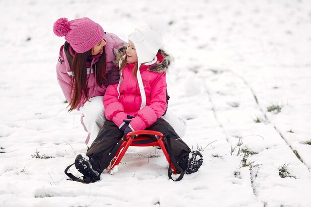 家族のクリスマス休暇にニットの冬の帽子をかぶった家族。公園の女性と少女。そりで遊ぶ人。