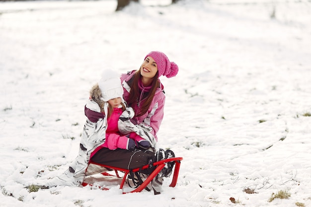 Family in knitted winter hats on family Christmas vacation. Woman and little girl in a park. People playing with sled.