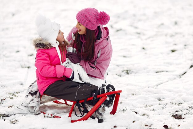Семья в вязаных зимних шапках на семейных рождественских каникулах. Женщина и маленькая девочка в парке. Люди играют с санками.