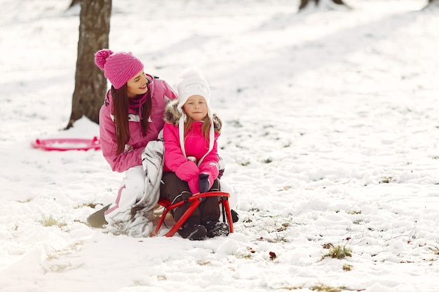 Family in knitted winter hats on family Christmas vacation. Woman and little girl in a park. People playing with sled.