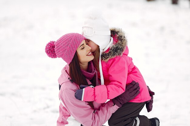 Family in knitted winter hats on family Christmas vacation. Woman and little girl in a park. People playing.