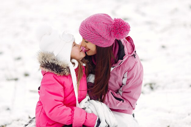 Family in knitted winter hats on family Christmas vacation. Woman and little girl in a park. People playing.