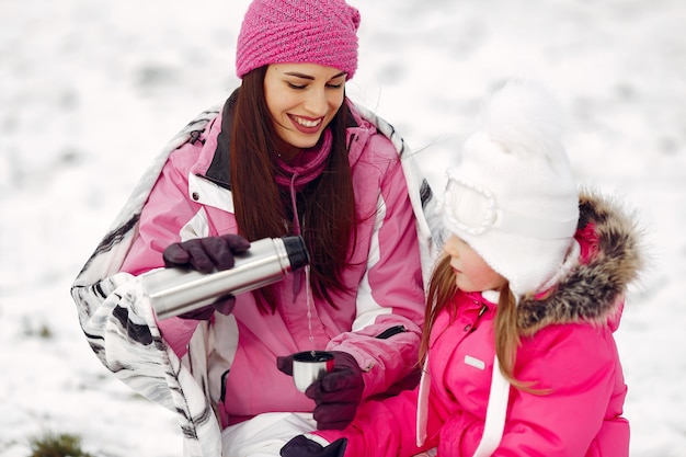 Family in knitted winter hats on family Christmas vacation. Woman and little girl in a park. People wit thermos.