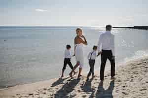 Foto gratuita la famiglia in abiti di lusso sta camminando a piedi nudi sulla spiaggia di sabbia in una calda giornata di sole