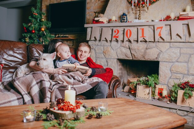 Family lying on a couch with a blanket while they read a book and a chimney in the background