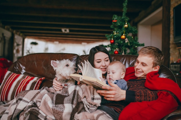 Family lying on a couch with a blanket while they read a book