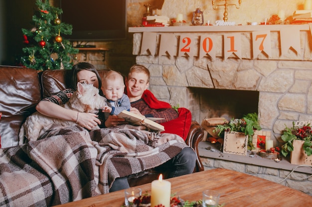 Famiglia sdraiata su un divano con una coperta mentre leggono un libro