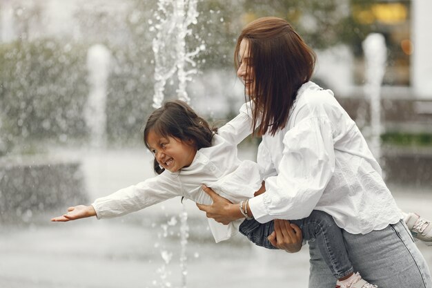 市の噴水の近くの家族。水で遊ぶ笑いを持つ母。