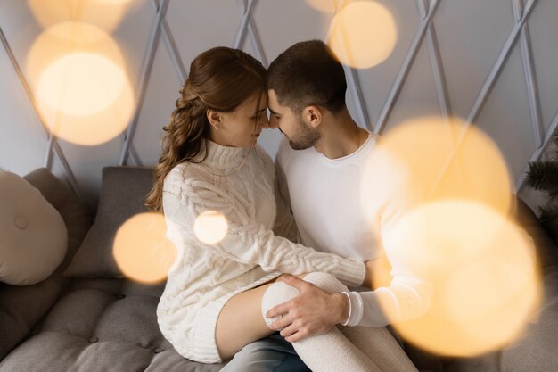 Family portrait. Man and woman relax on soft grey bad in a room with Christmas tree