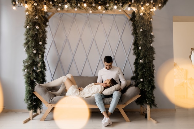 Family portrait. Man and woman relax on soft grey bad in a room with Christmas tree