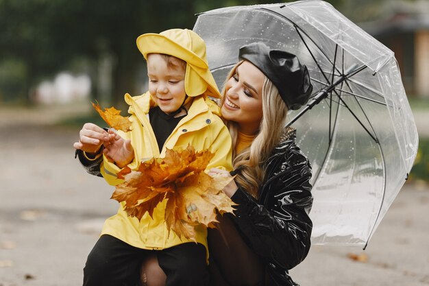비오는 공원에서 가족. 노란 비옷을 입은 아이와 검은 코트를 입은 여자.