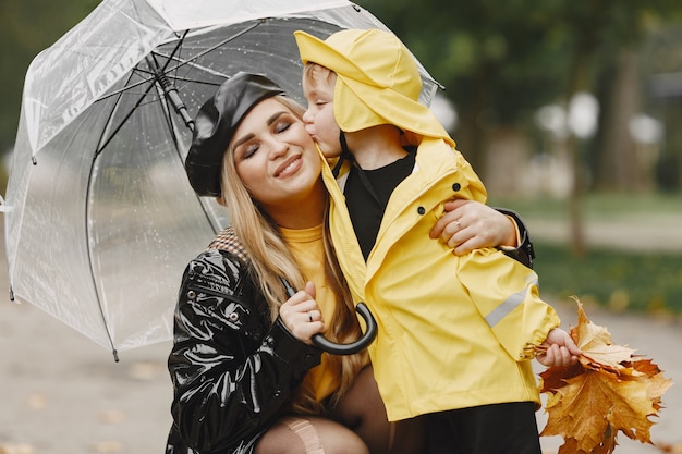 Семья в дождливом парке. Малыш в желтых плащах и женщина в черном пальто.