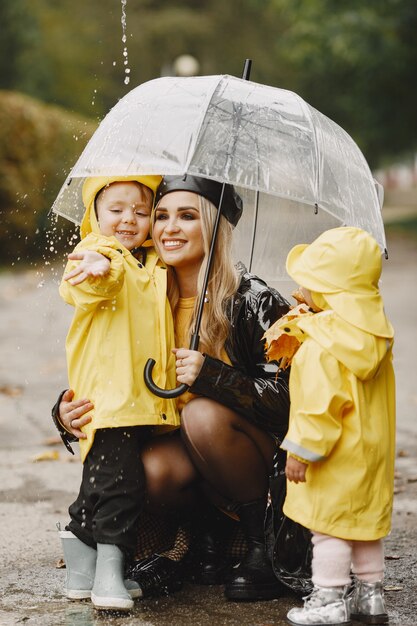 Family in a rainy park. Kids in a yellow raincoats and woman in a black coat.
