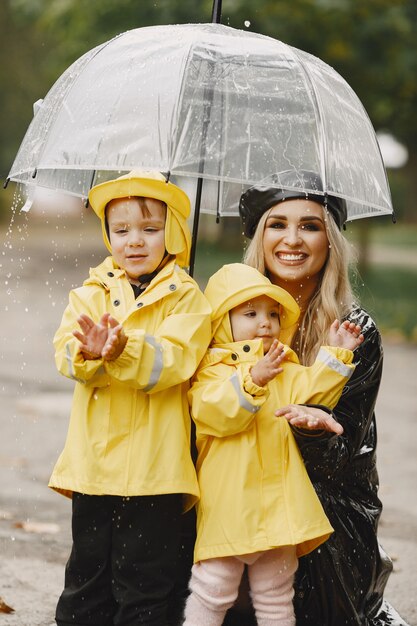 Family in a rainy park. Kids in a yellow raincoats and woman in a black coat.