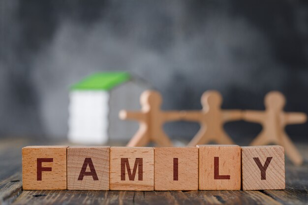 Family safety concept with wooden figures of people, cubes, model house side view.