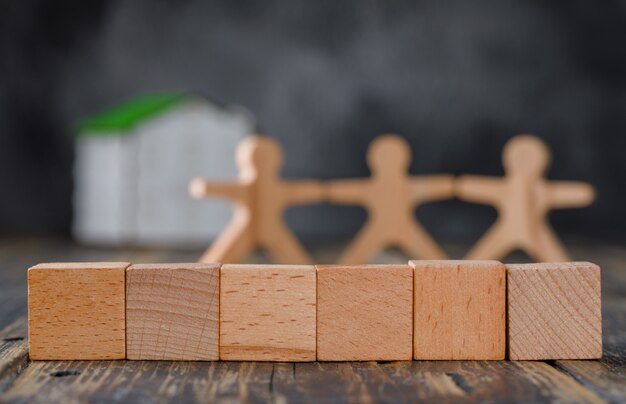 Family safety concept with wooden figures of people, cubes, model house side view.