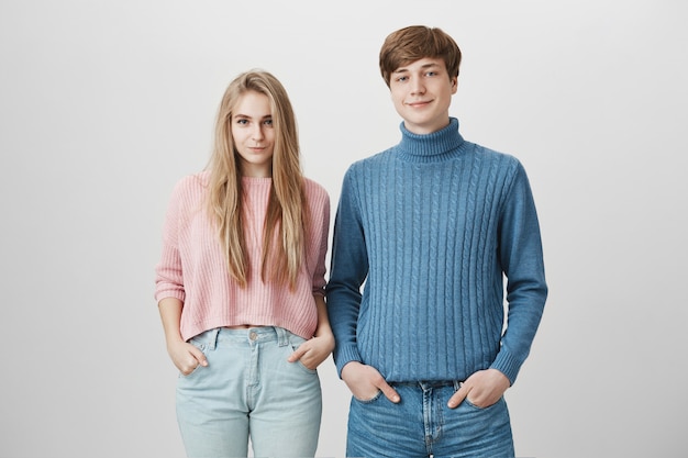 Free photo family shot of caucasian brother and sister standing close to each other posing indoors in colourful knitted sweaters
