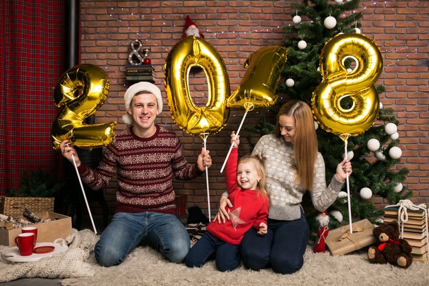 Family sitting by the Christmas tree holding 2018 balloons