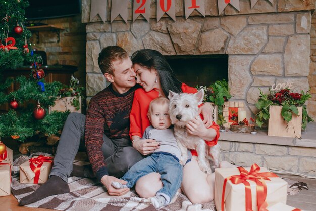 Family sitting in front of the fireplace with their baby and their dog and a christmas tree