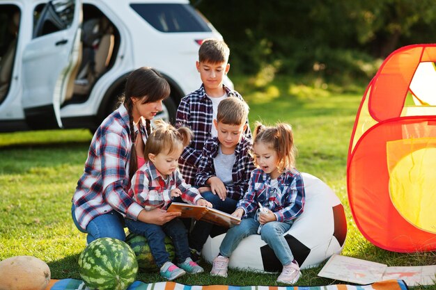 Family spending time together Mother reading book outdoor with kids against their suv car
