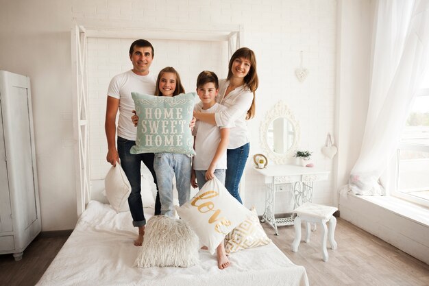 Family standing on bed with holding home sweet home text on pillow