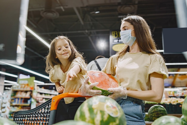 Family at the supermarket. Woman in a protective mask. People choose vegetables. Mother with daughter. Coronavirus.