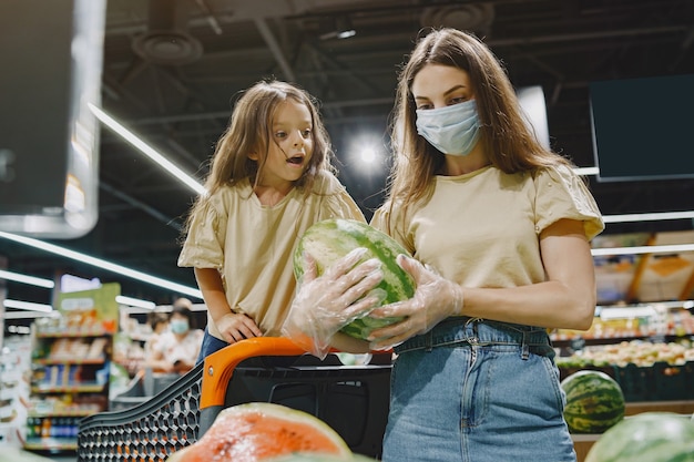 スーパーマーケットの家族。保護マスクの女性。人々は野菜を選びます。娘と母。コロナウイルス。