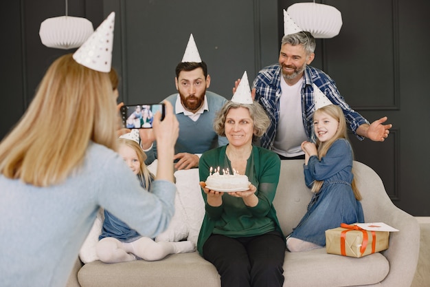 Family and two their daughters celebrate birthdayTwo men and two little girl sitting on a sofa Mother is taking a photo of them