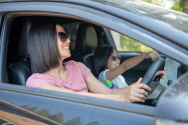 家族での休暇、車での遠征中の幸せな家族、娘が横に座っている間に車を運転する母親、母親と娘が旅行している。夏の自動車乗り。