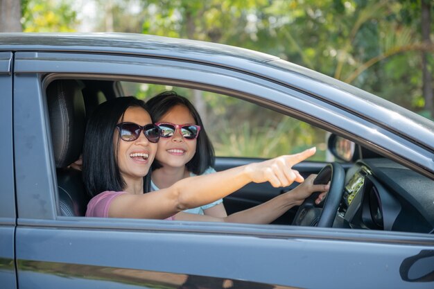 家族での休暇、車での遠征中の幸せな家族、娘が横に座っている間に車を運転する母親、母親と娘が旅行している。夏の自動車乗り。