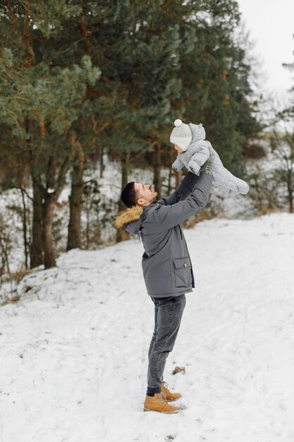 明るい日に冬の公園で楽しんで雪の中を歩いている家族が抱き合って笑っている