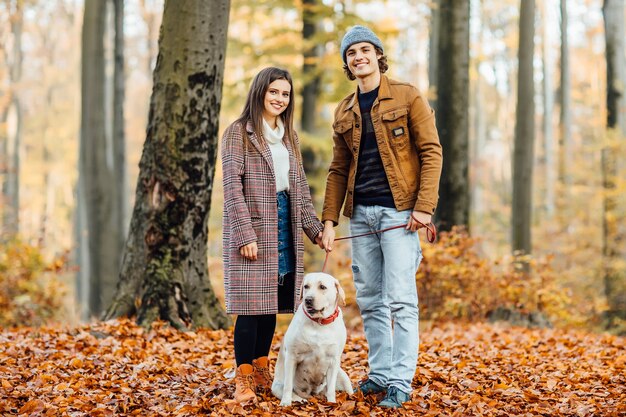 Family walking with golden labrador in red collar in autumn park