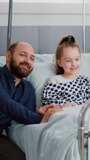 Семья смотрит мультфильм по телевизору в больничной палате в ожидании медицинской экспертизы во время медицинского осмотра. Больной ребенок-пациент отдыхает в постели после хирургической операции