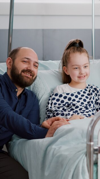 Family watching cartoon movie on television in hospital ward while waiting for medical sickness expertise during healthcare examination. Sick child patient resting in bed after medicine surgery