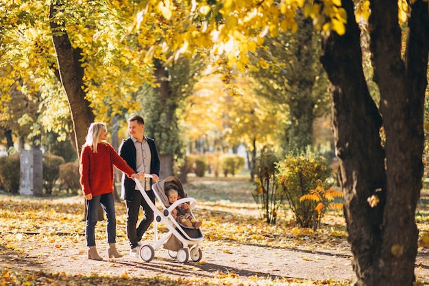 Семья с дочерью в детской коляске гуляет по осеннему парку