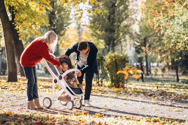 Family with baby daugher in a baby carriage walking an autumn park