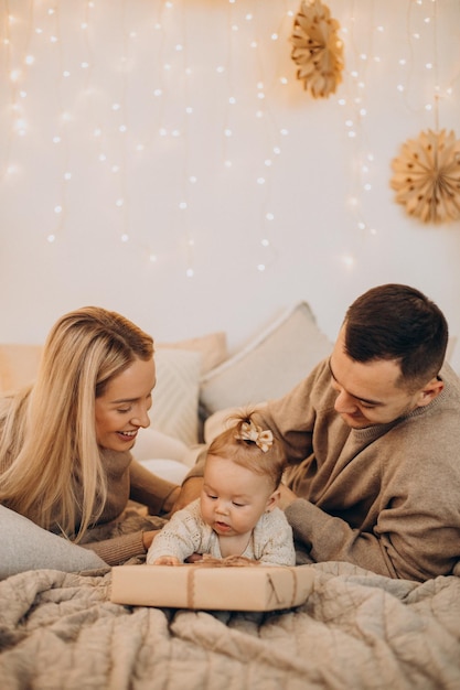 Family with baby daughter lying on bed with Christmas presents