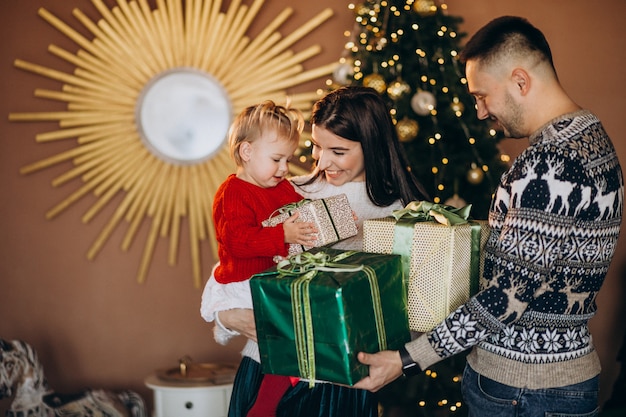 Family with little daughter by Christmas tree unpacking gift box