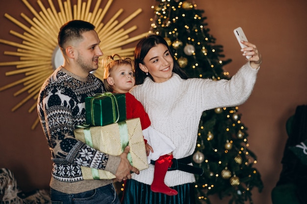 Family with little daughter by Christmas tree unpacking gift box